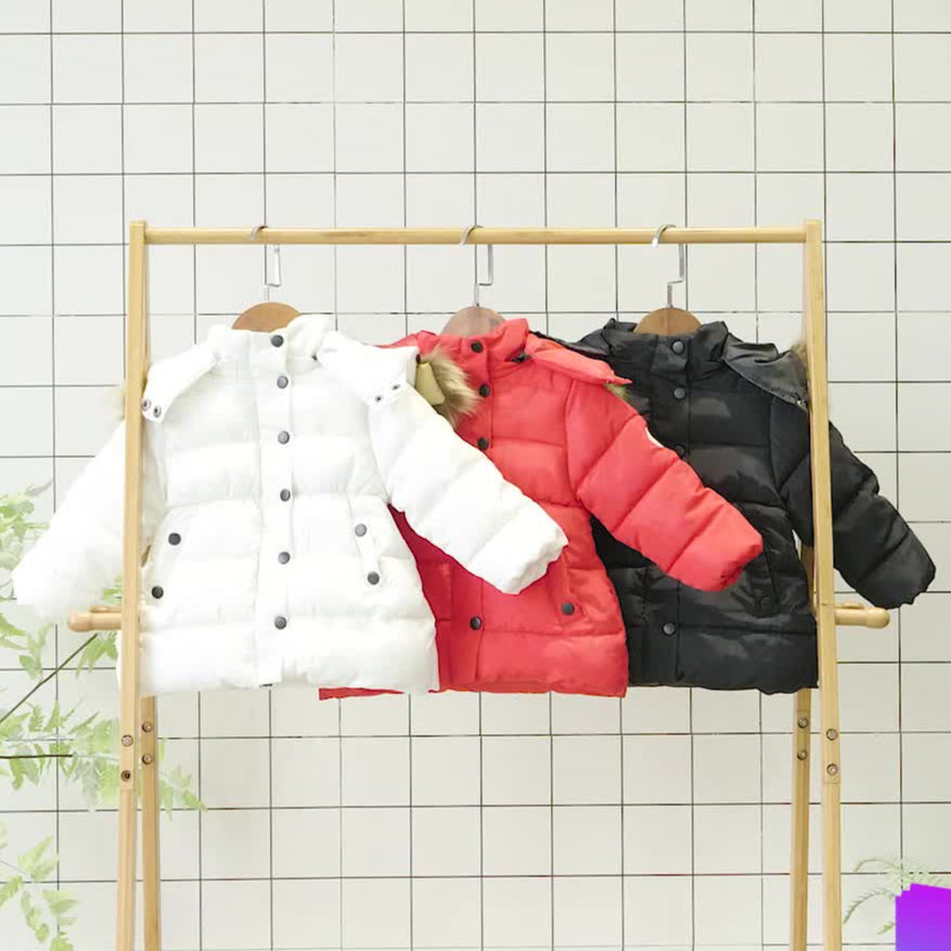 Three girls's jackets in white, red, and black hanging on a wooden rack against a tiled wall.